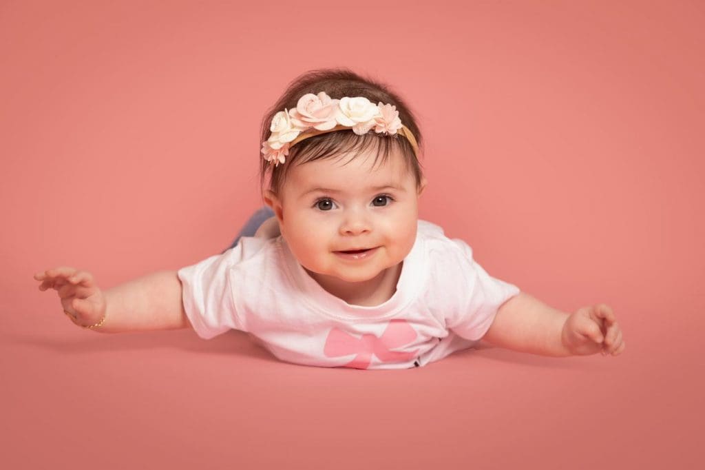 Smiling baby girl lying on her tummy with arms outstretched during a professional baby photoshoot in Birmingham.