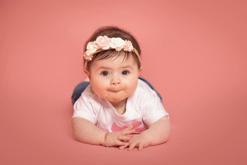 Baby girl lying on her tummy with hands together during a professional baby photoshoot in Birmingham.