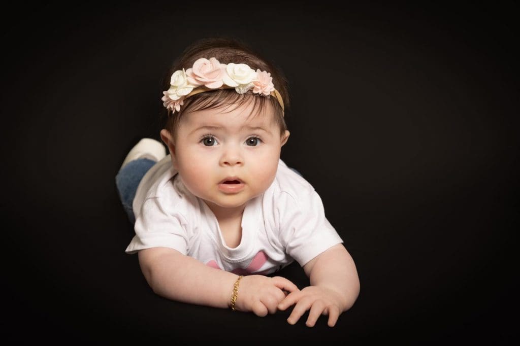 Baby girl lying on her tummy against a dark background during a professional baby photoshoot in Birmingham.