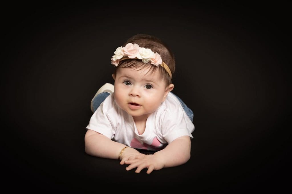 Baby girl lying on her tummy and looking toward the camera during a professional baby photoshoot in Birmingham.