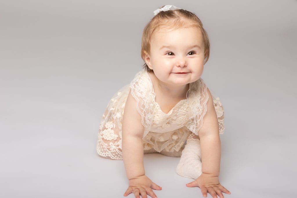 Baby girl crawling forward and smiling in a lace dress during a professional baby photoshoot in Birmingham.