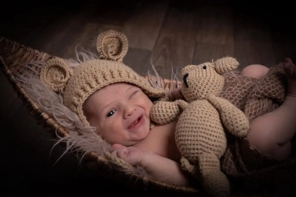 smiling newborn baby portrait in Birmingham photography studio lying in basket with teddy bear