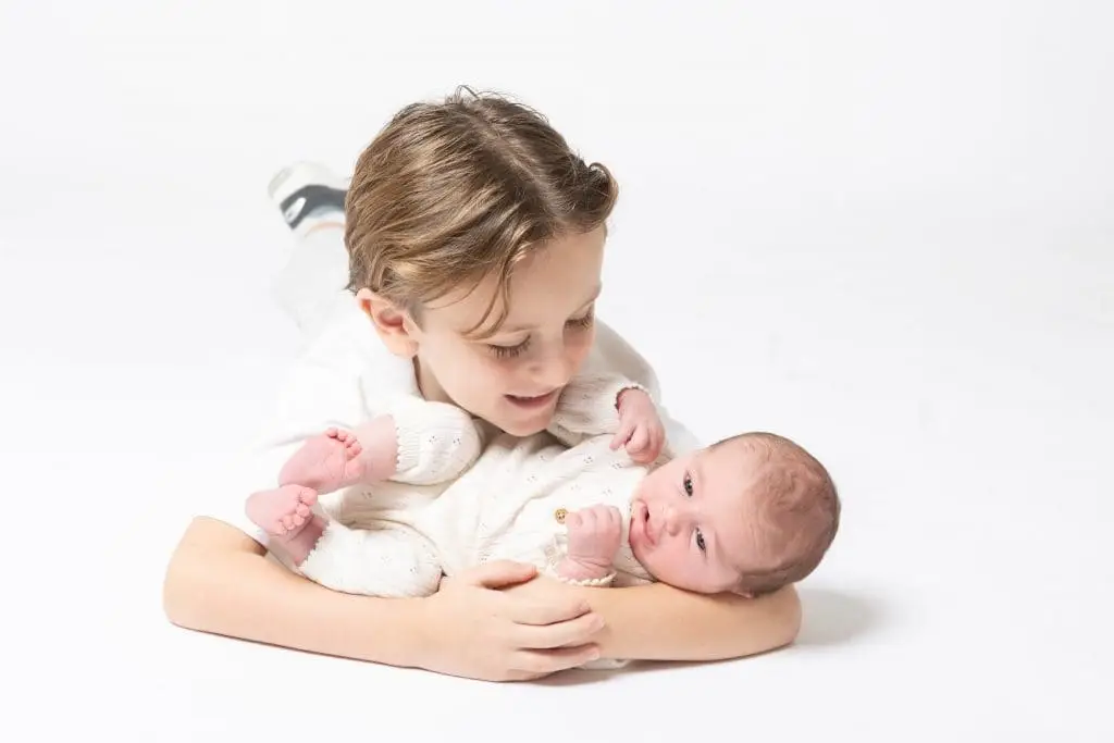 newborn baby with older sibling during Birmingham newborn photography studio session on white background