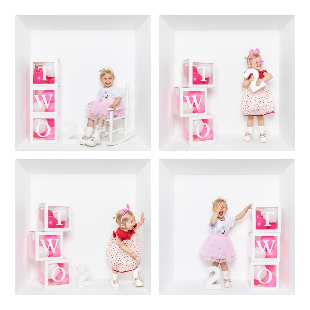 Four young girls pose in white cube frames with pink and white blocks that spell TWO and the number 2, each wearing festive outfits and celebrating a second birthday—a delightful moment expertly captured by a Birmingham inside the box photographer.