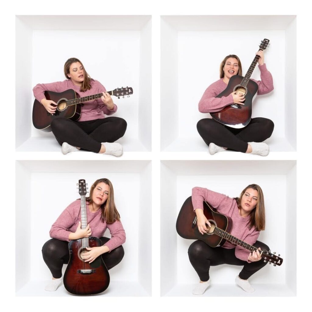 A woman in a pink jumper and black leggings, captured by a Birmingham inside the box photographer, plays an acoustic guitar in various poses inside a white, box-like space, appearing thoughtful and expressive in each of the four panels.