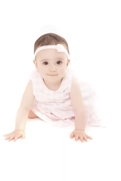 A baby wearing a white dress and a white headband with a flower, crawling on a white background.