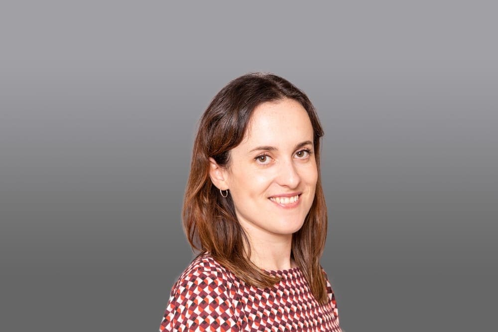 A woman with shoulder-length brown hair wearing a patterned top smiles at the camera in front of a plain grey background, captured by a Birmingham commercial photographer.