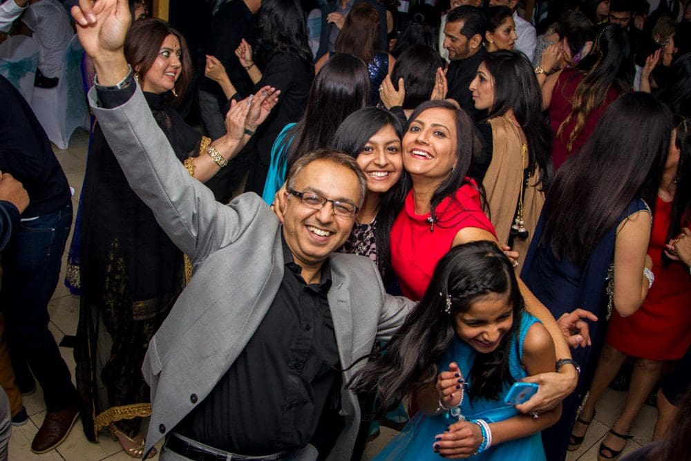 A group of people at a lively party, smiling and posing for the camera. Captured by a talented Birmingham event photographer, a man in glasses raises his arm in excitement, whilst others around him laugh and enjoy the celebration.