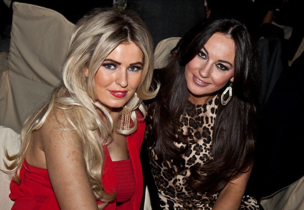 Two women posing together at an event, one with long blonde hair in a red dress, and the other with long dark hair in a leopard print outfit. Both are smiling and wearing statement earrings, perfectly captured by a skilled Birmingham event photographer.